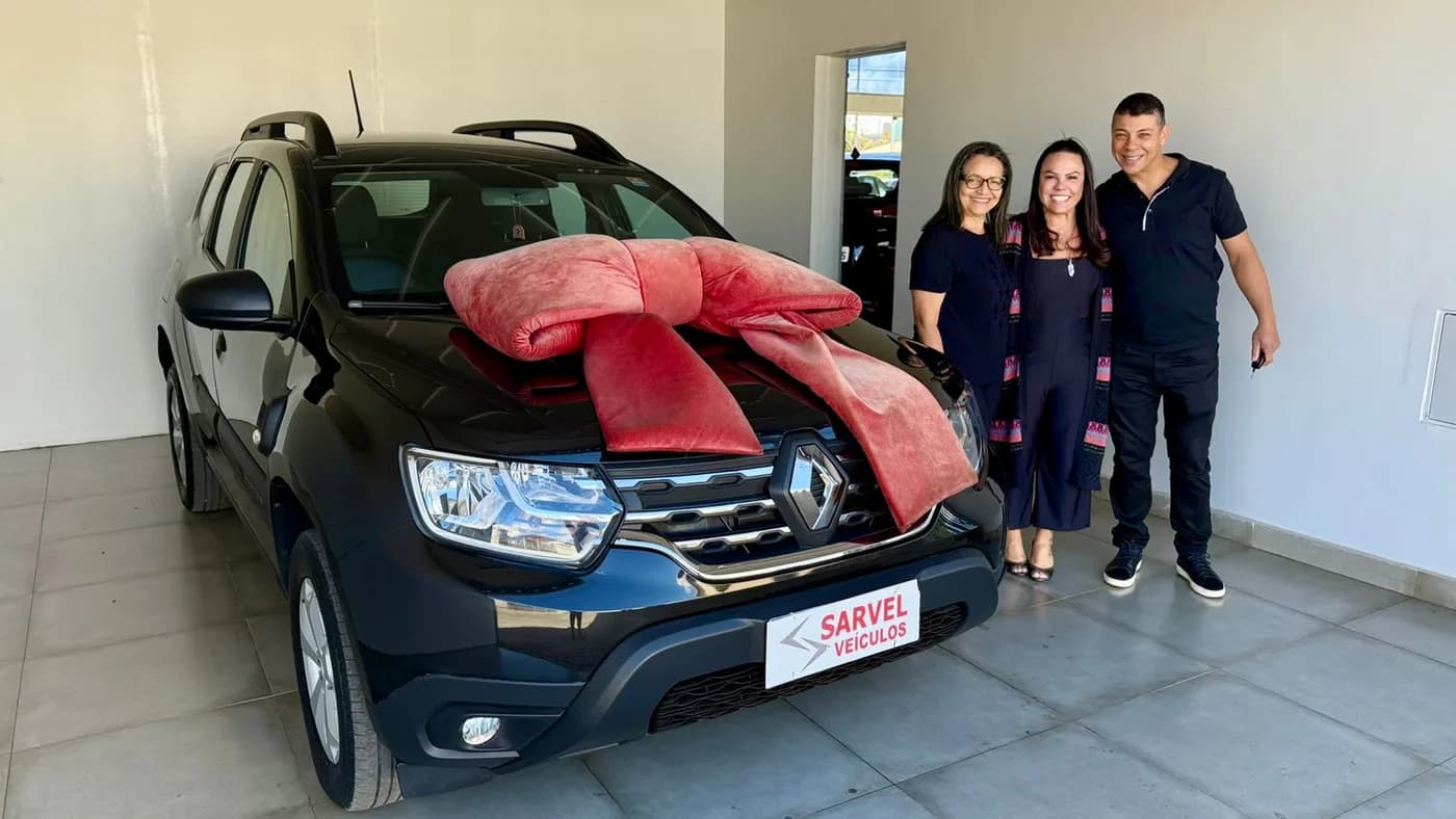 Família de três pessoas ao lado de um SUV cinza com laço vermelho, em concessionária