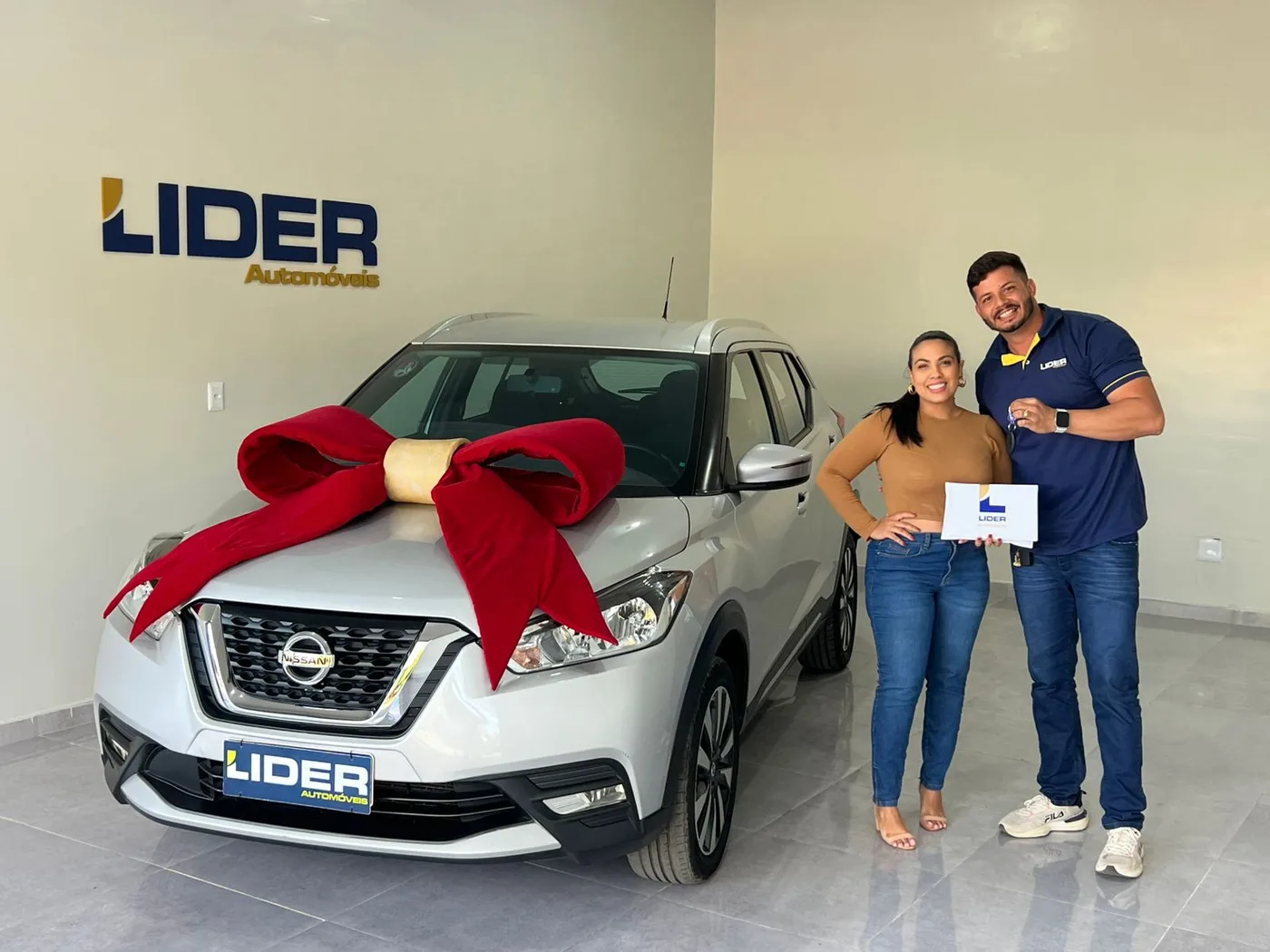 Consultora e cliente comemorando ao lado de um carro branco com laço vermelho