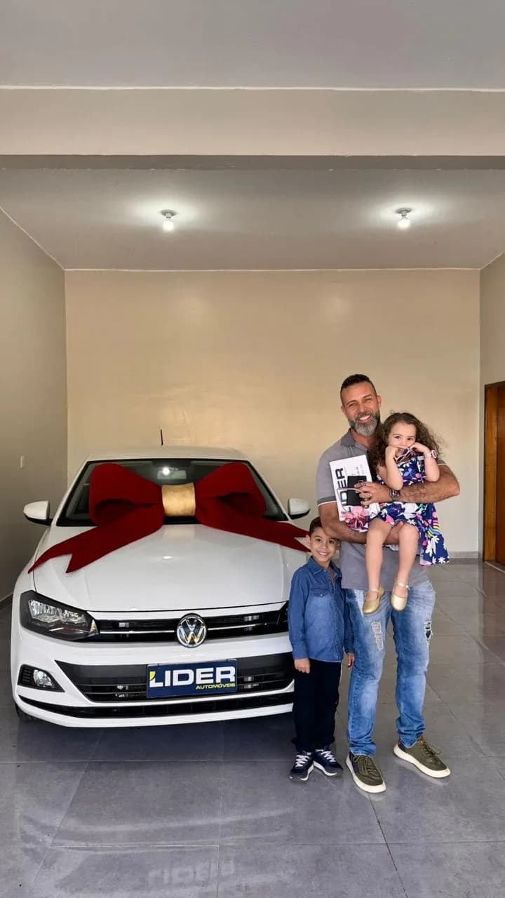 Família com criança ao lado de um carro branco com laço vermelho, em concessionária